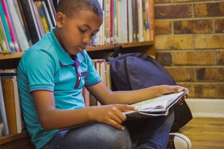 boy reading book by bookcase