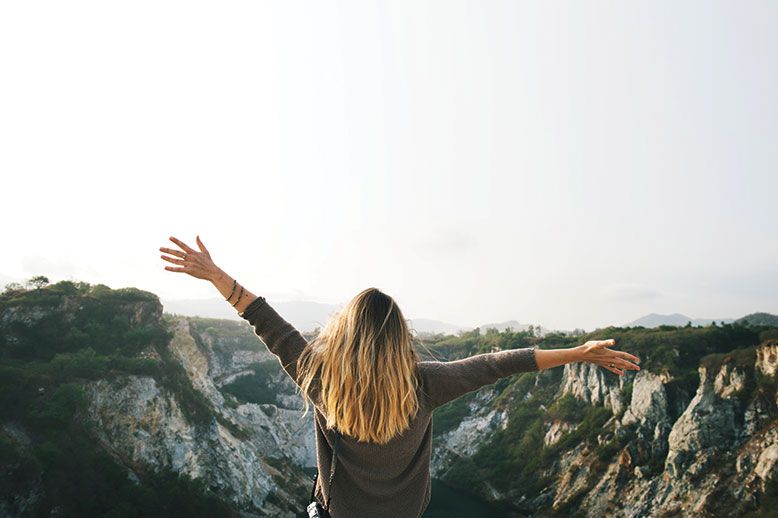 woman spreading arms facing a mountain range cliff