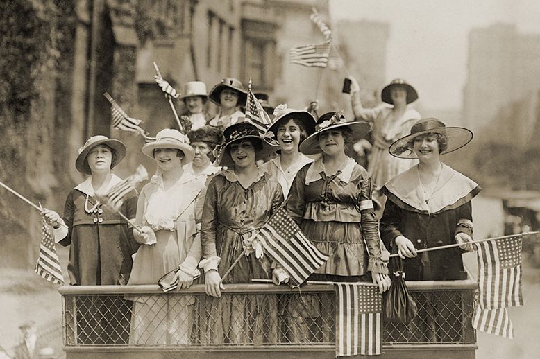 archival photo of women waving American flags at New York City parade circa 1911