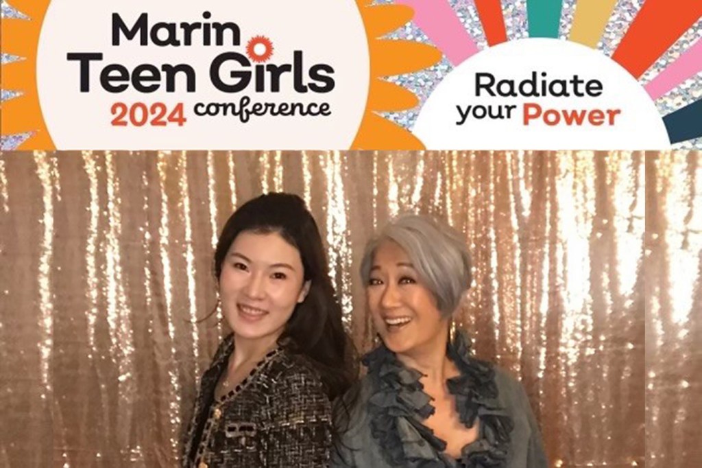 Two women are posing for a photo together. The woman on the left has long  dark brown hair and brown eyes and is wearing a black and gold jacket. She is RBC Wealth Management client associate Jessica Yu. The woman on the right is financial advisor Helen Abe. Helen has short grey hair and brown eyes and is wearing a dark green ruffled top. Both women are smiling. They are standing in front of a sparkly gold backdrop.