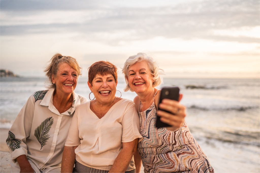 senior female friends taking selfie on beach