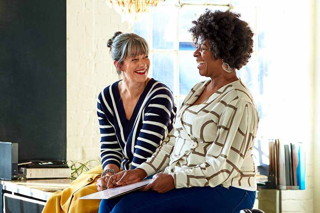 two generation X female friends laughing together at home